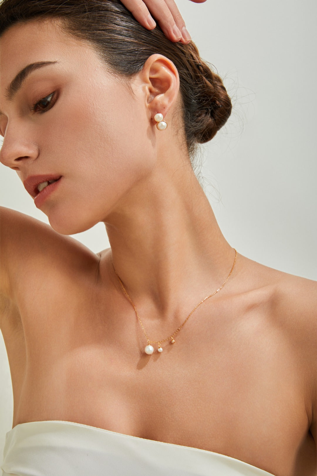 A woman wearing a flowing white dress and a delicate pearl necklace, exuding elegance and charm.