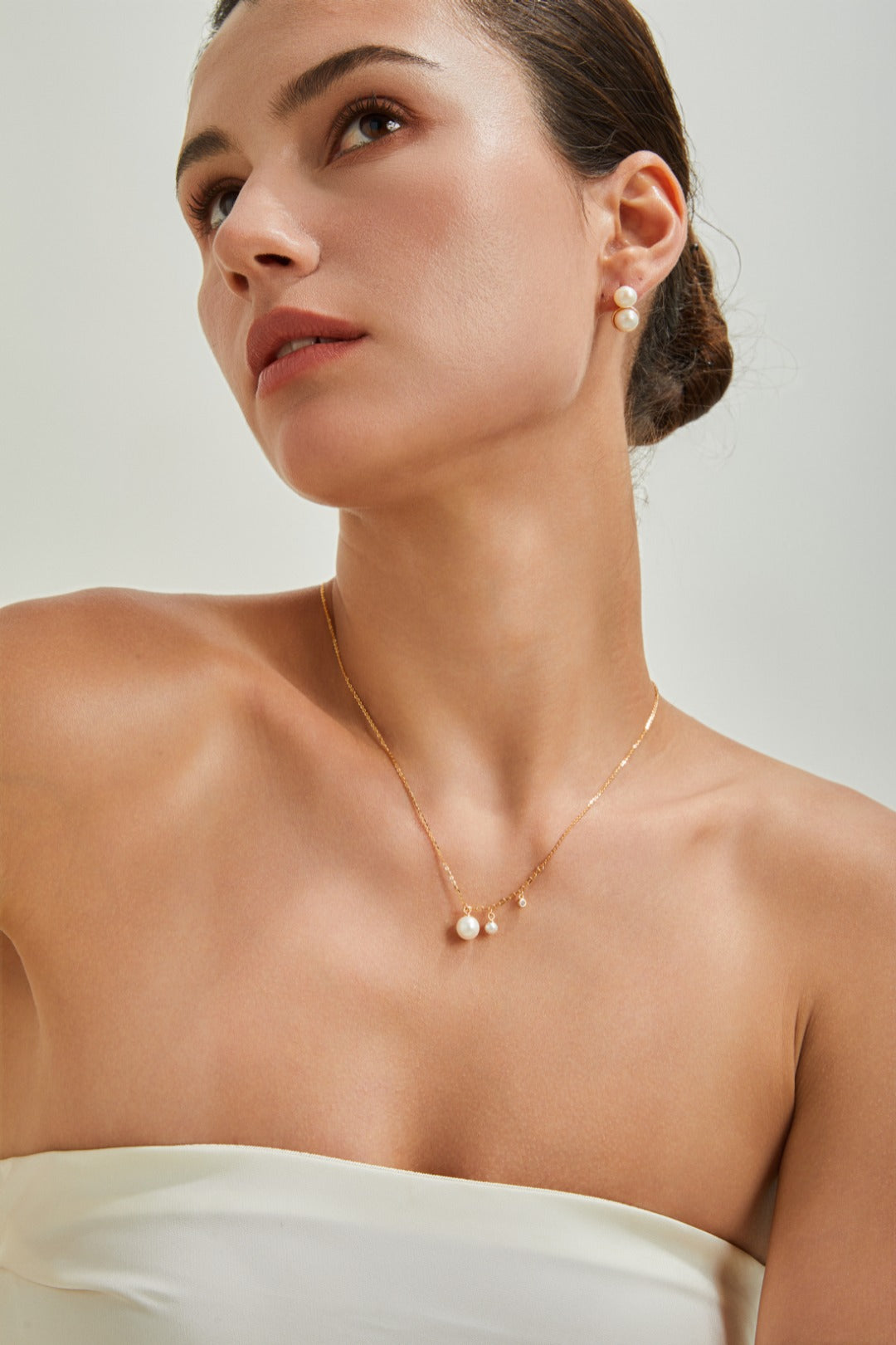 A woman in a white dress adorned with a gold necklace, standing gracefully with a serene expression.