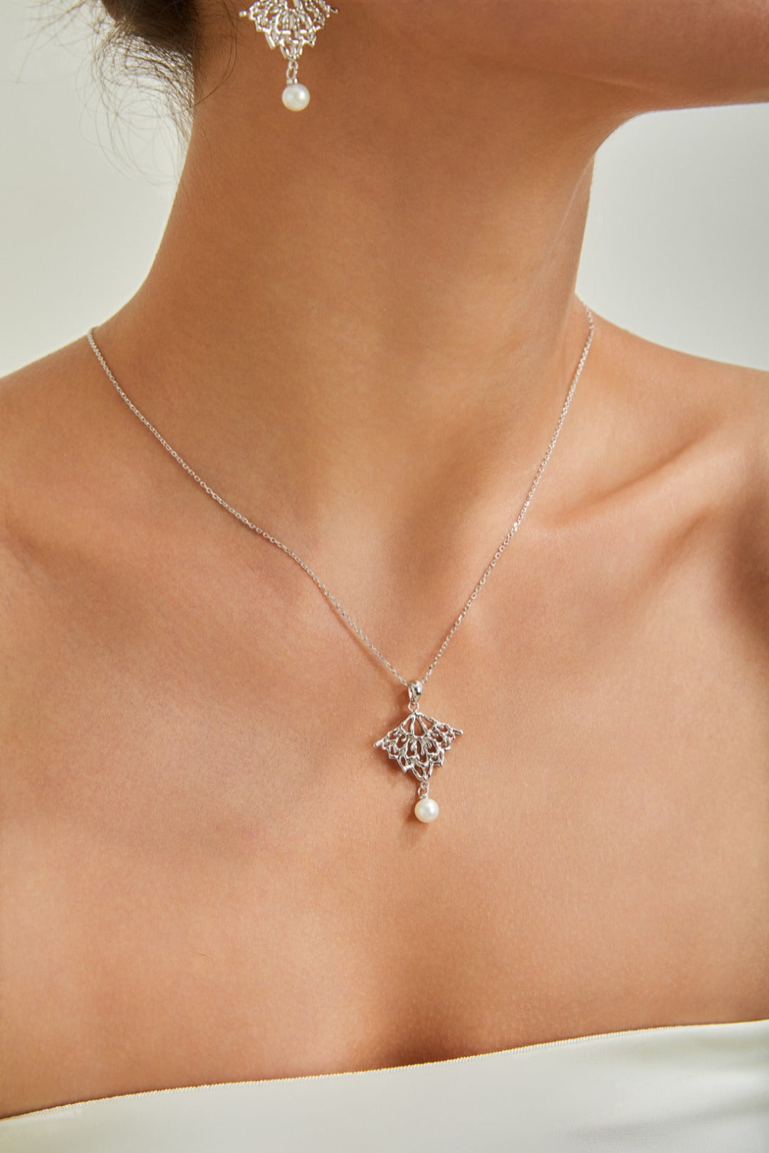 A woman dressed in white, featuring a striking diamond and pearl necklace that adds a touch of luxury to her outfit.