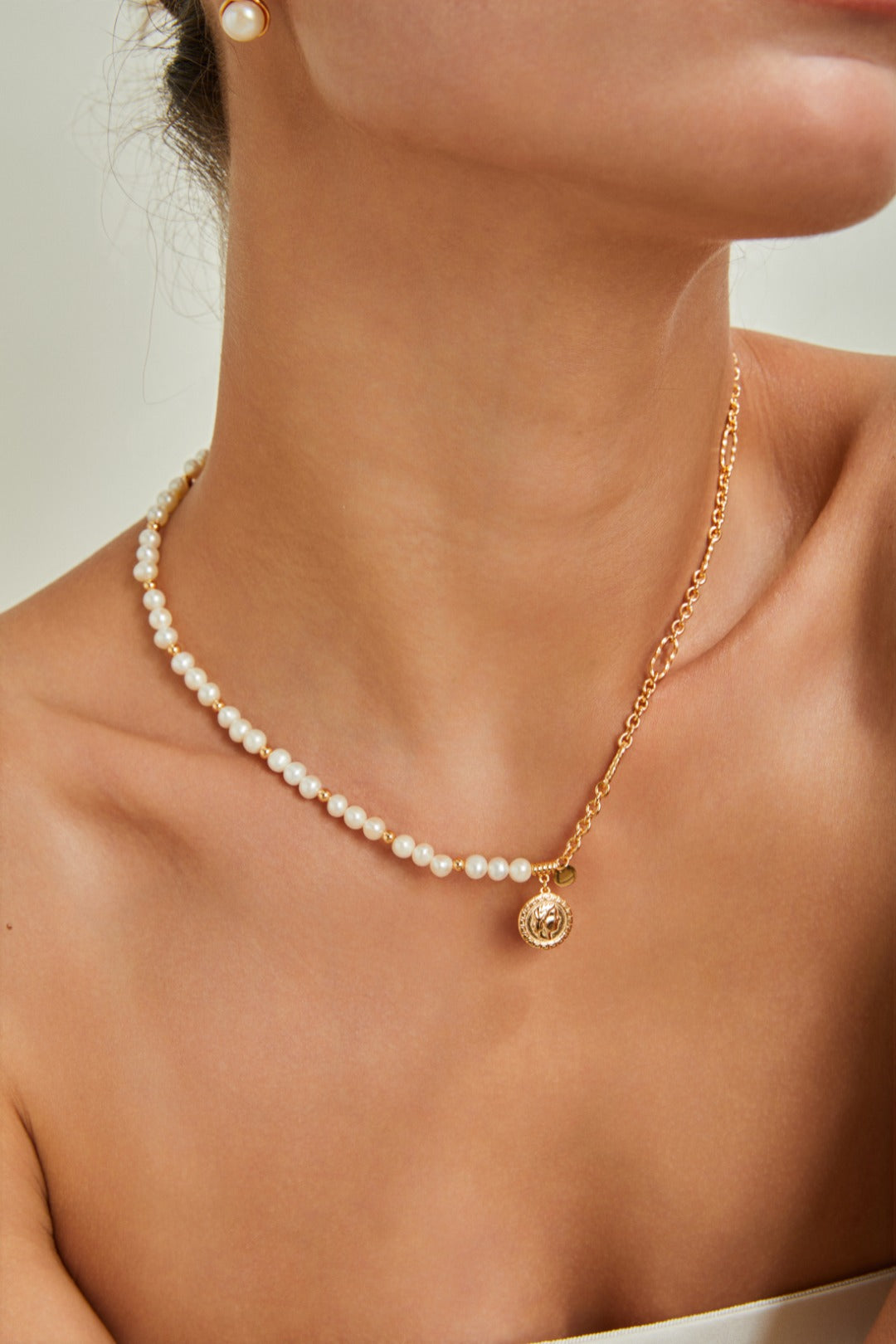 A woman displays a stunning gold necklace featuring a delicate pearl chain.