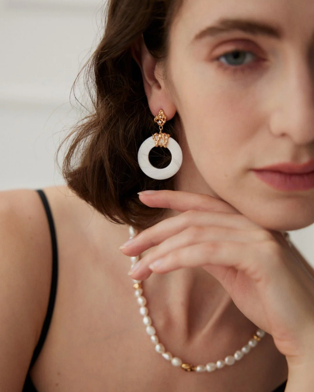 A woman displaying elegance with a white pearl necklace and pearl shell earrings, highlighting her sophisticated fashion choice.