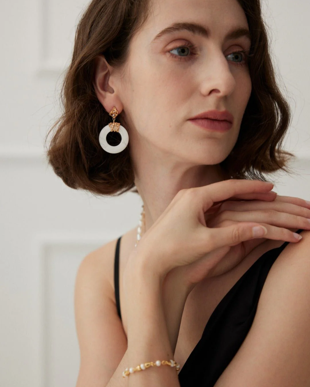 A woman in a sleek black dress, complemented by elegant white pearl shell earrings, radiating style and elegance.