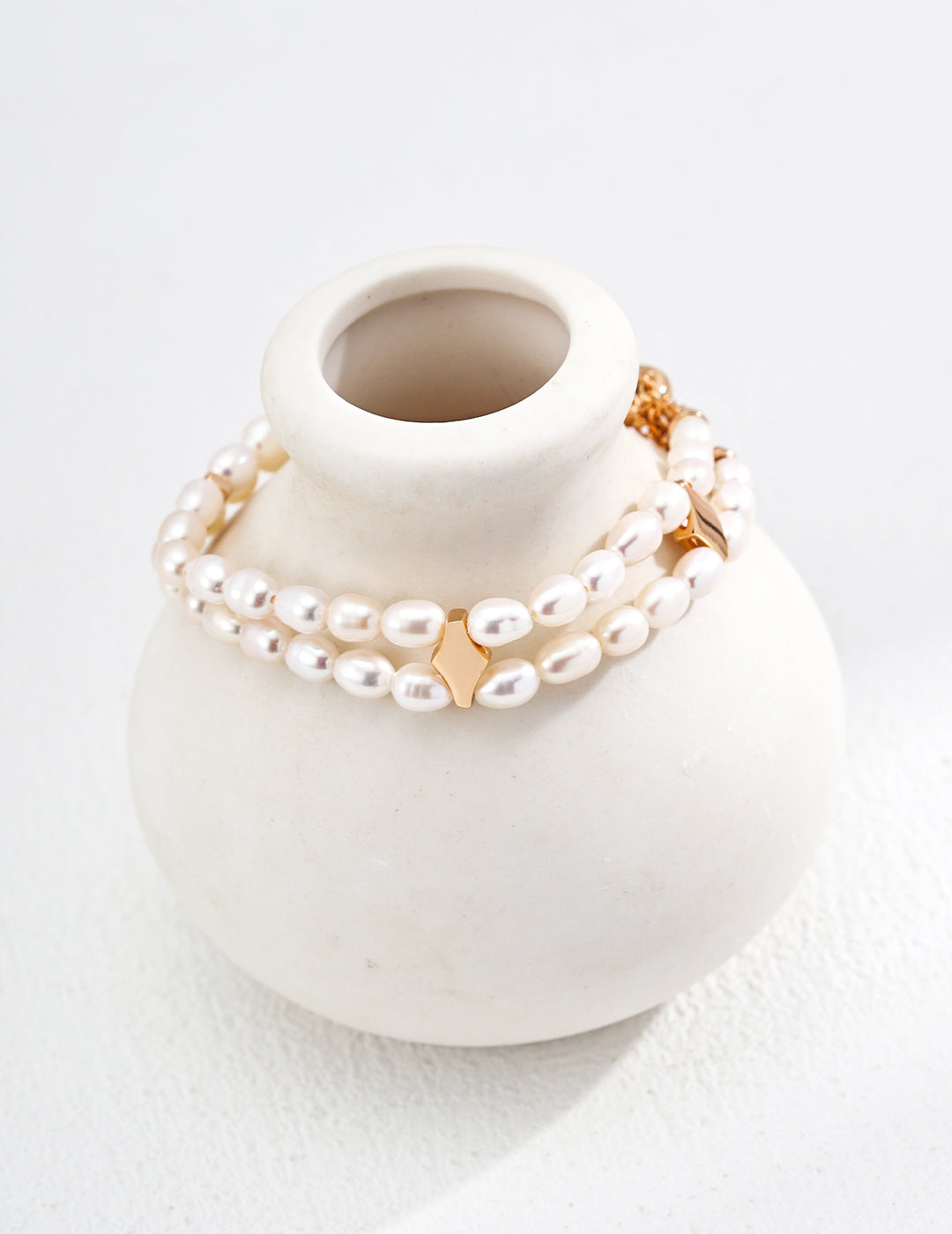 A white vase features a white stone alongside a celestial gold bracelet, showcasing a minimalist yet stylish arrangement.