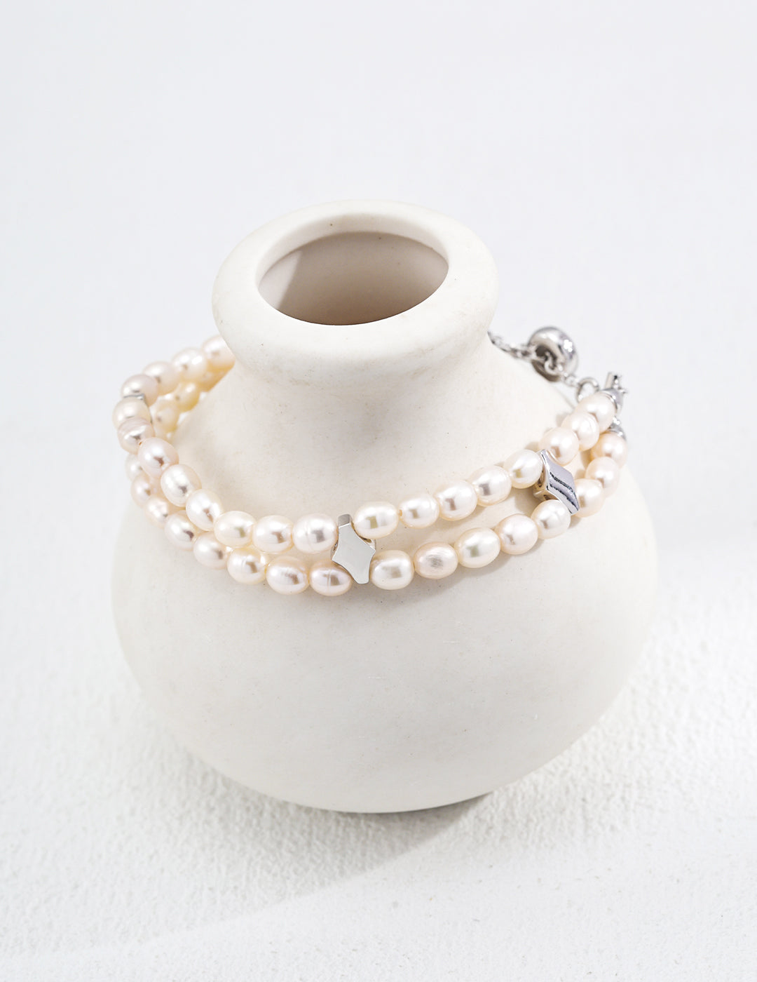 A minimalist white vase featuring a white stone and a celestial pearl bracelet, embodying purity and grace.
