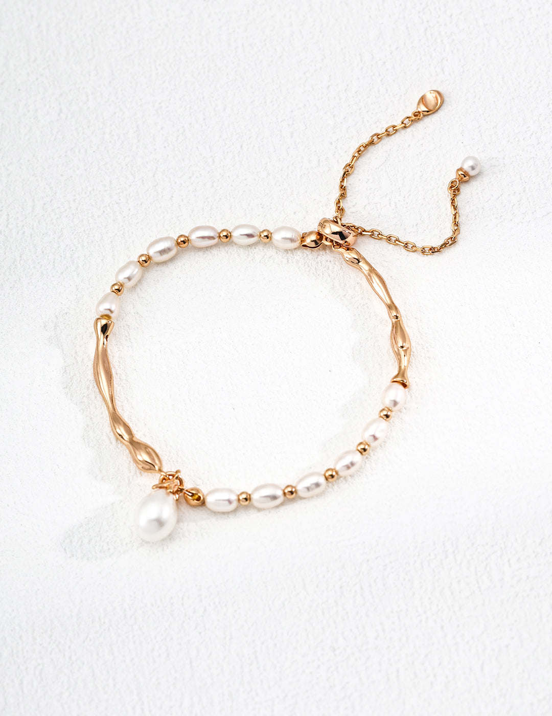 A delicate bracelet featuring white pearls and gold plated beads on a textured white background. It has a thin, adjustable chain with an elegant tone.