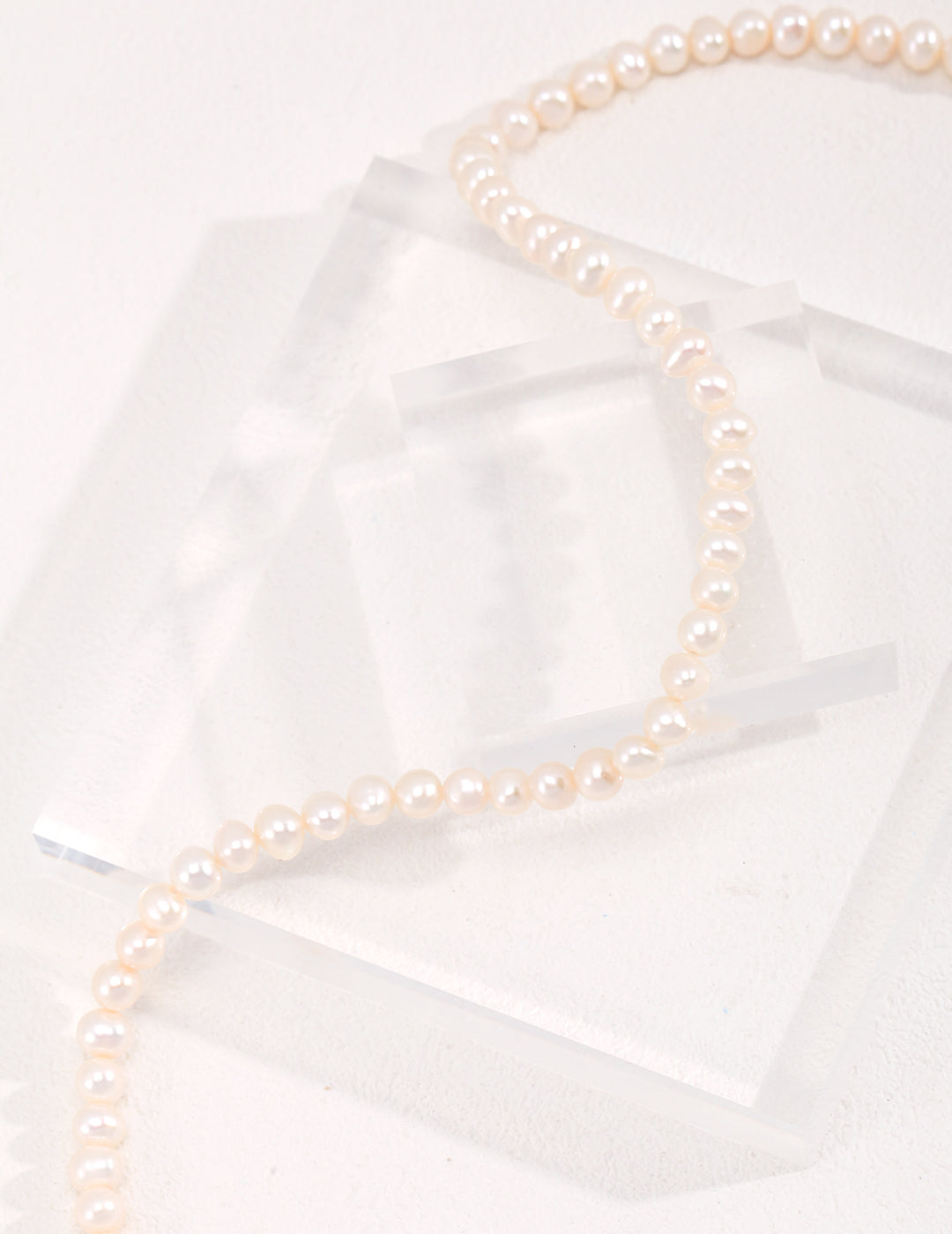 Stylish freshwater pearls arranged neatly on transparent surface.