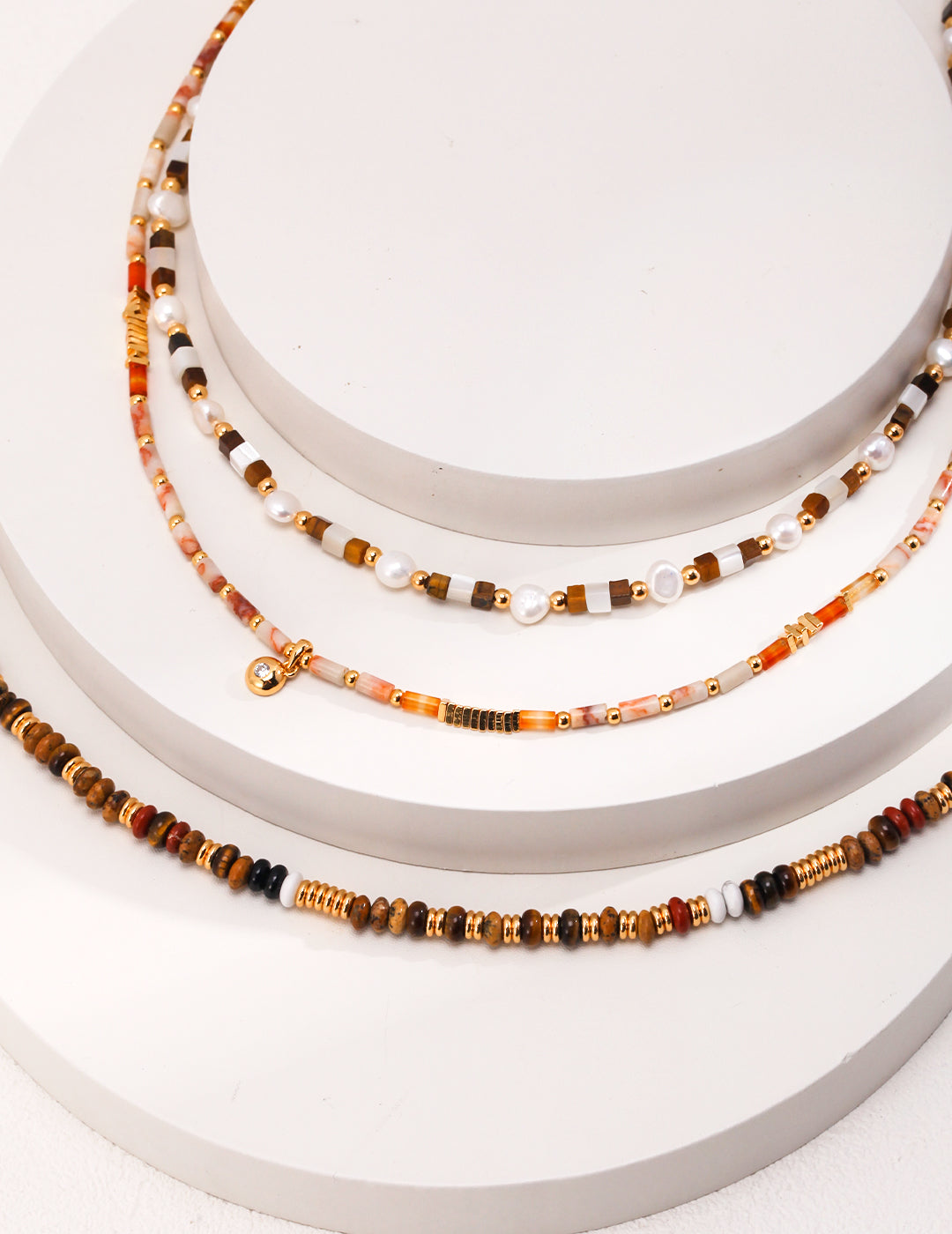 Three layered necklaces with beads and gold chains, featuring colorful gemstones on each layer.