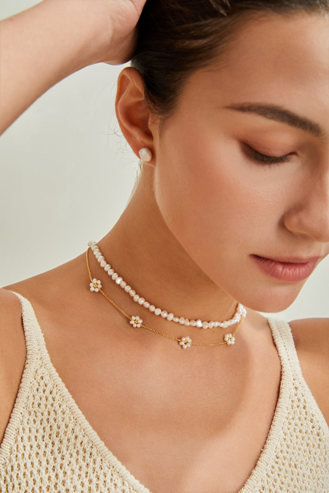 A woman in a white tank top elegantly wears a pearl petal necklace, highlighting her graceful and fashionable look.