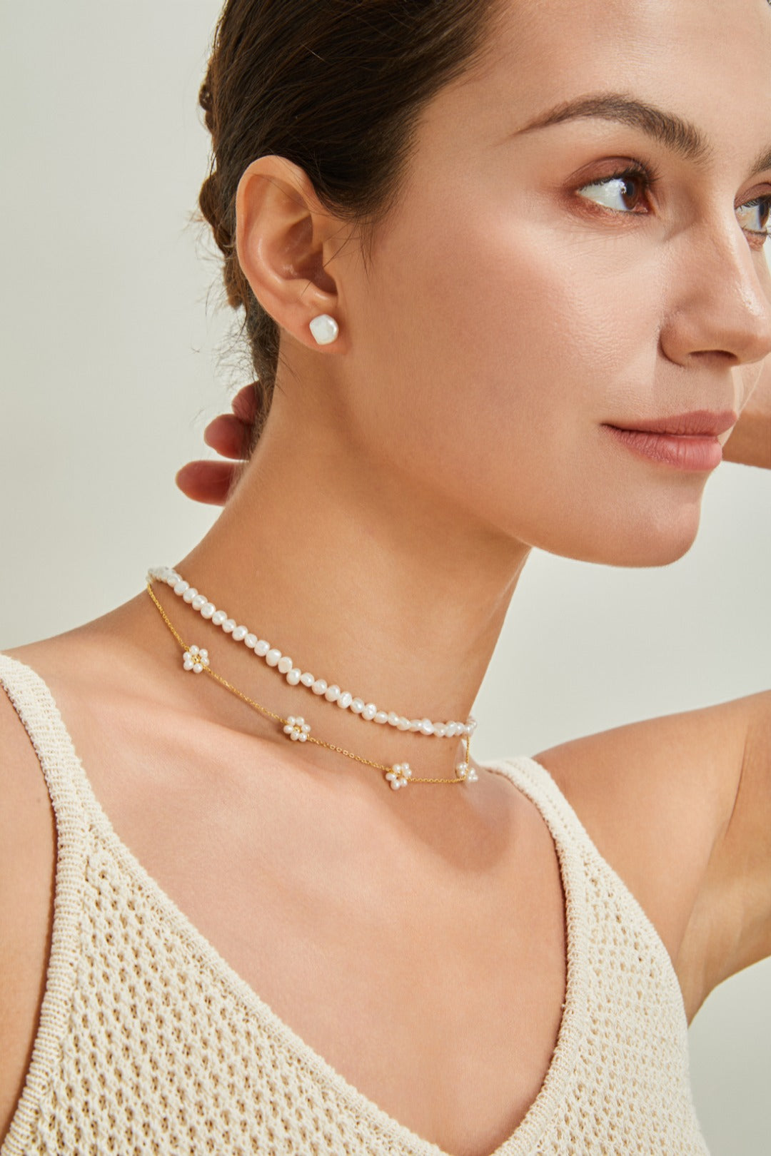 A woman in a white tank top showcases a stunning pearl petal necklace, exuding elegance and style.