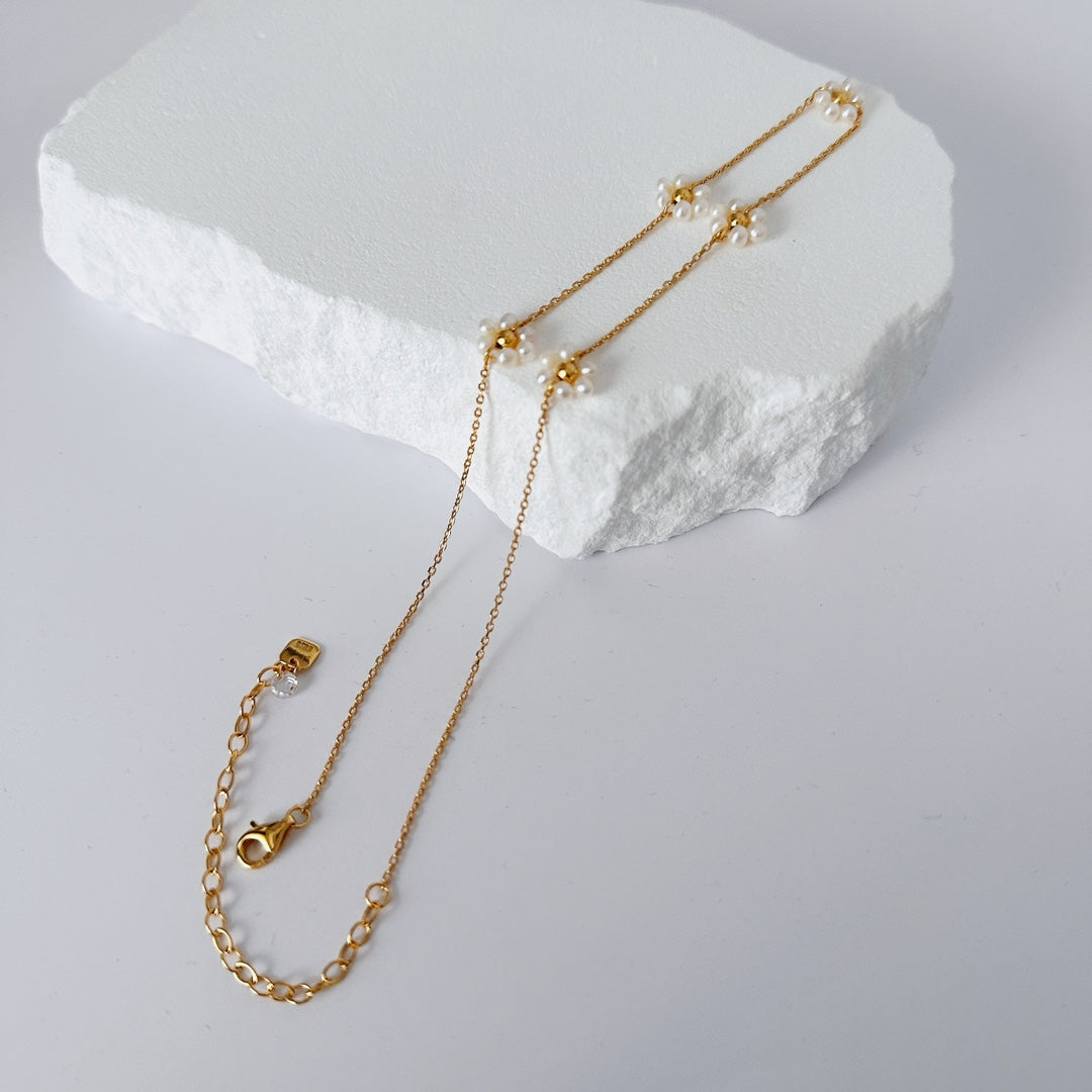 A stunning gold chain necklace lies on a white rock, highlighting its intricate pearl petal details in a serene setting.