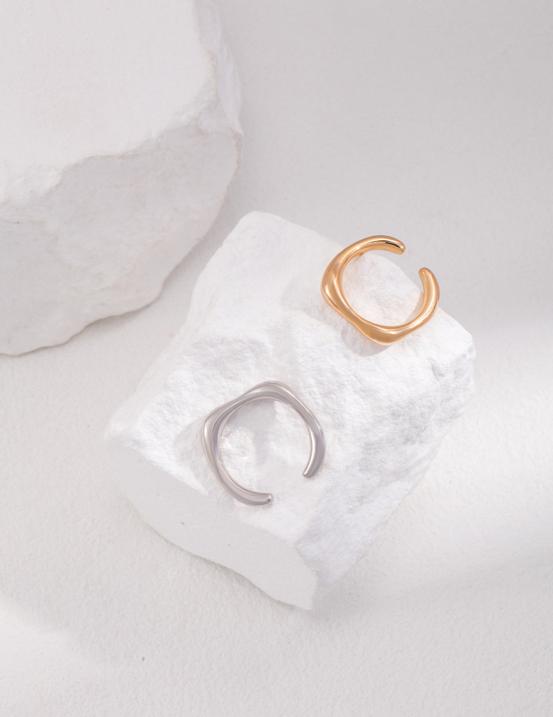 Minimalist silver and gold rings placed on a white rock.