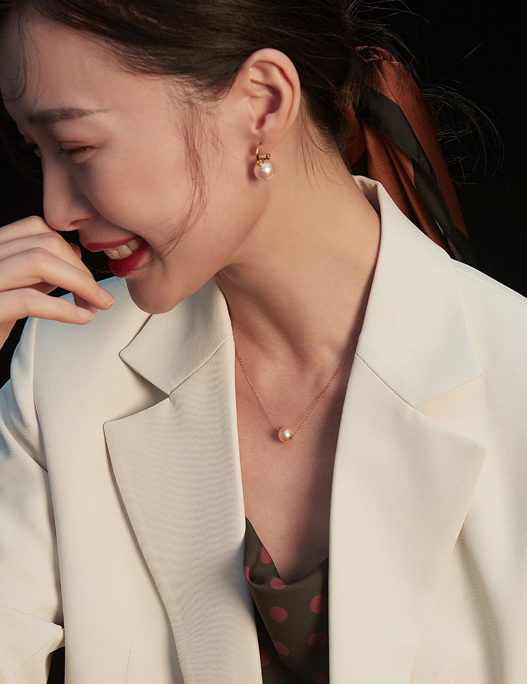 Stylish woman in a white blazer and polka dot shirt, complemented by a karat gold freshwater pearl necklace.