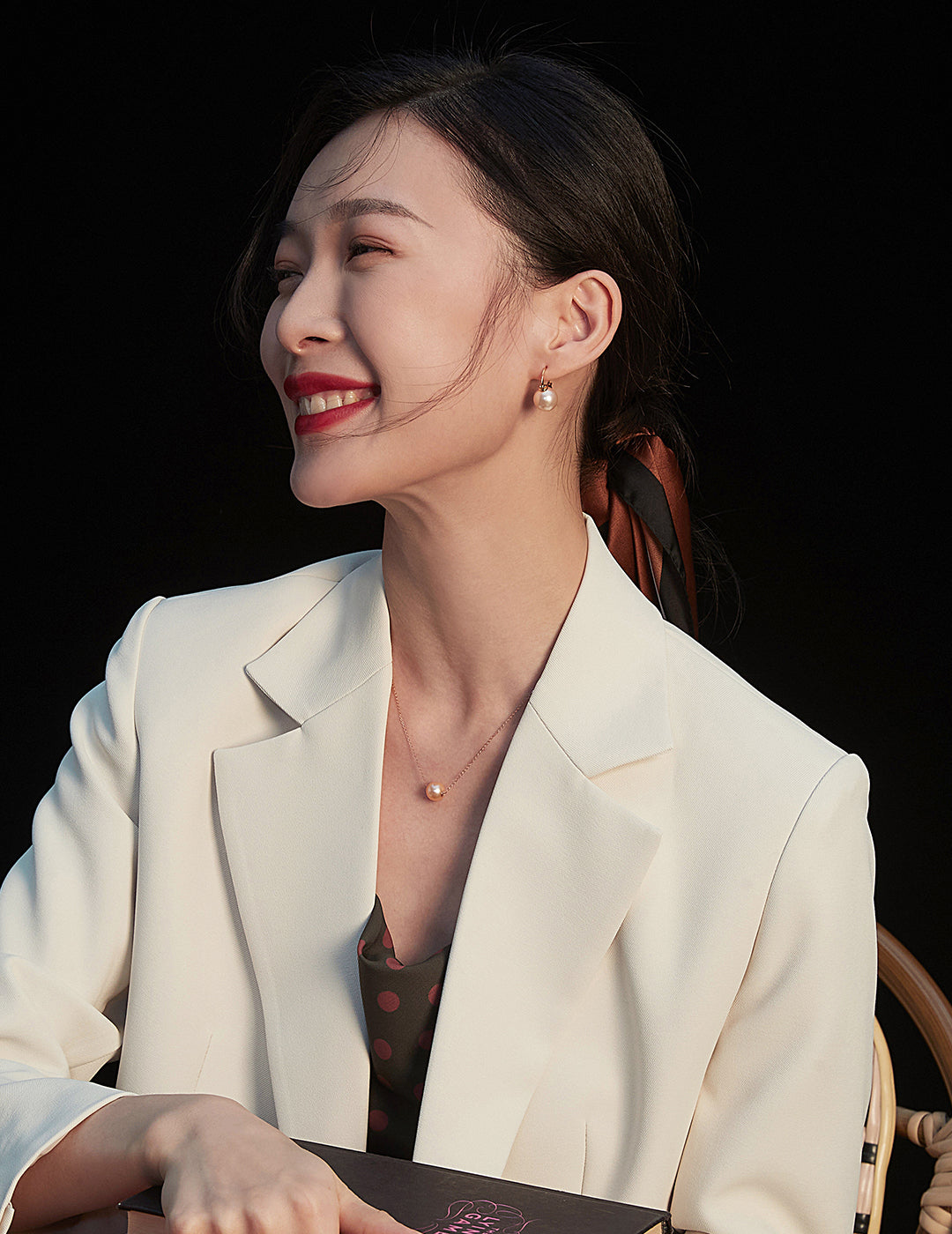 A woman wearing a white blazer and black top, featuring a stunning karat gold freshwater pearl necklace, showcases refined fashion.