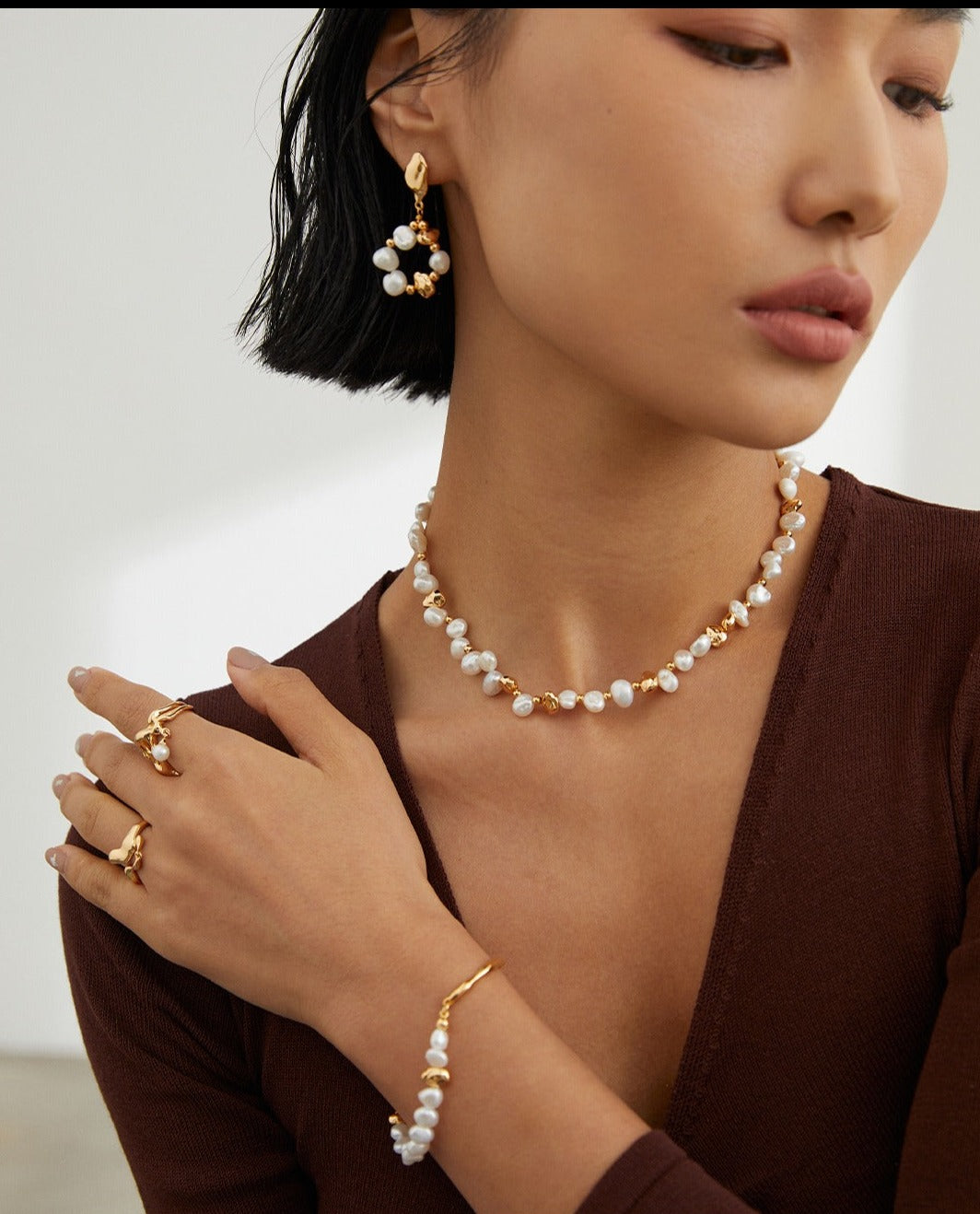 A model wearing a gold necklace and earrings set with freshwater pearls.