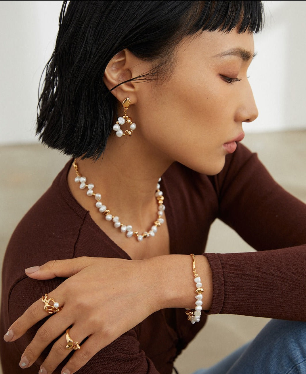 A model showcasing a gold necklace and earrings with freshwater pearls, complemented by a matching bracelet.