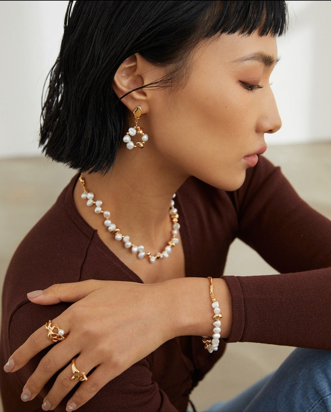 Model wearing a gold necklace and earrings, adorned with pearls, adding elegance to her attire.