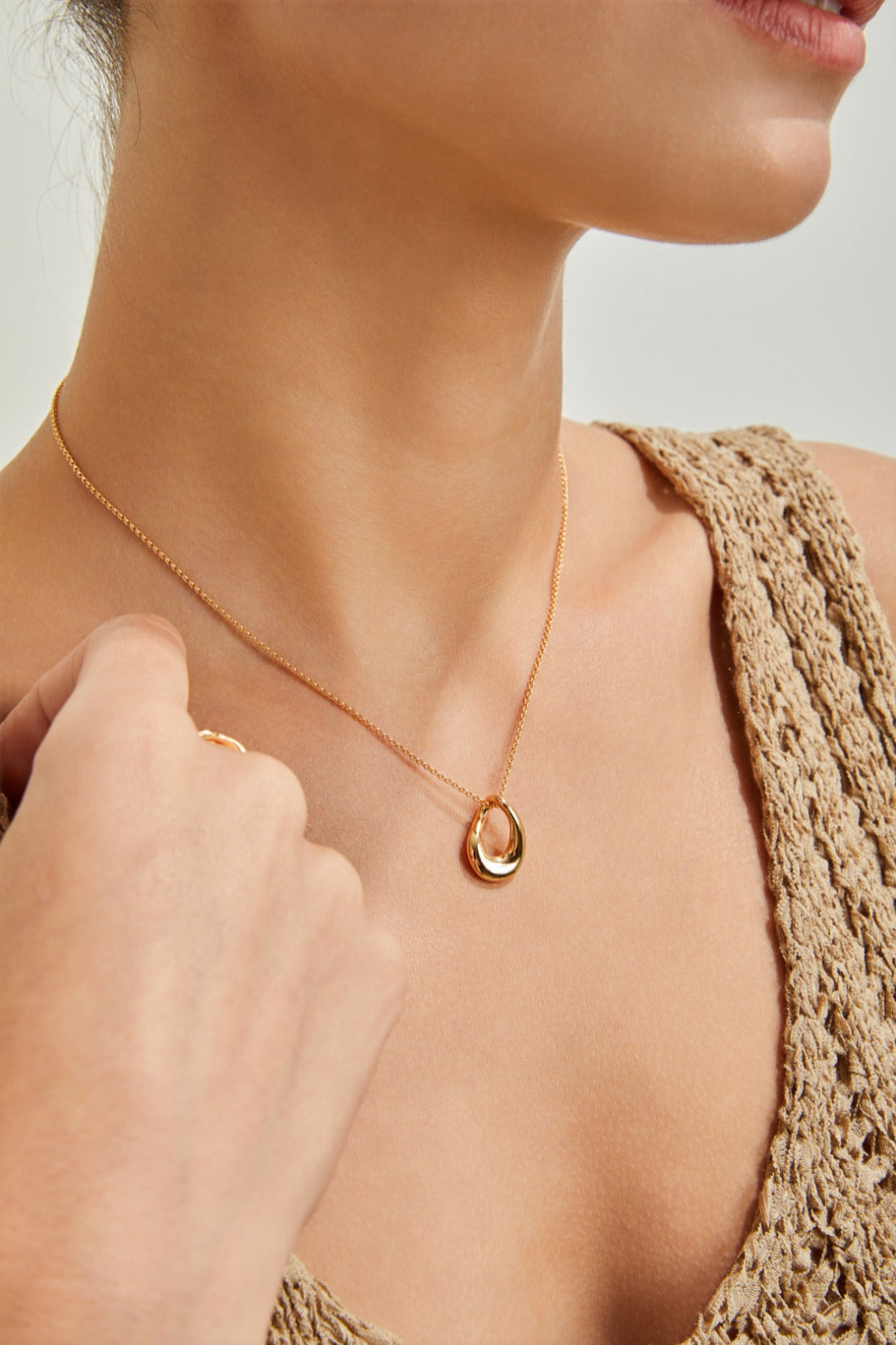 A woman displays a gold necklace with a circular pendant, emphasizing her chic and refined style.