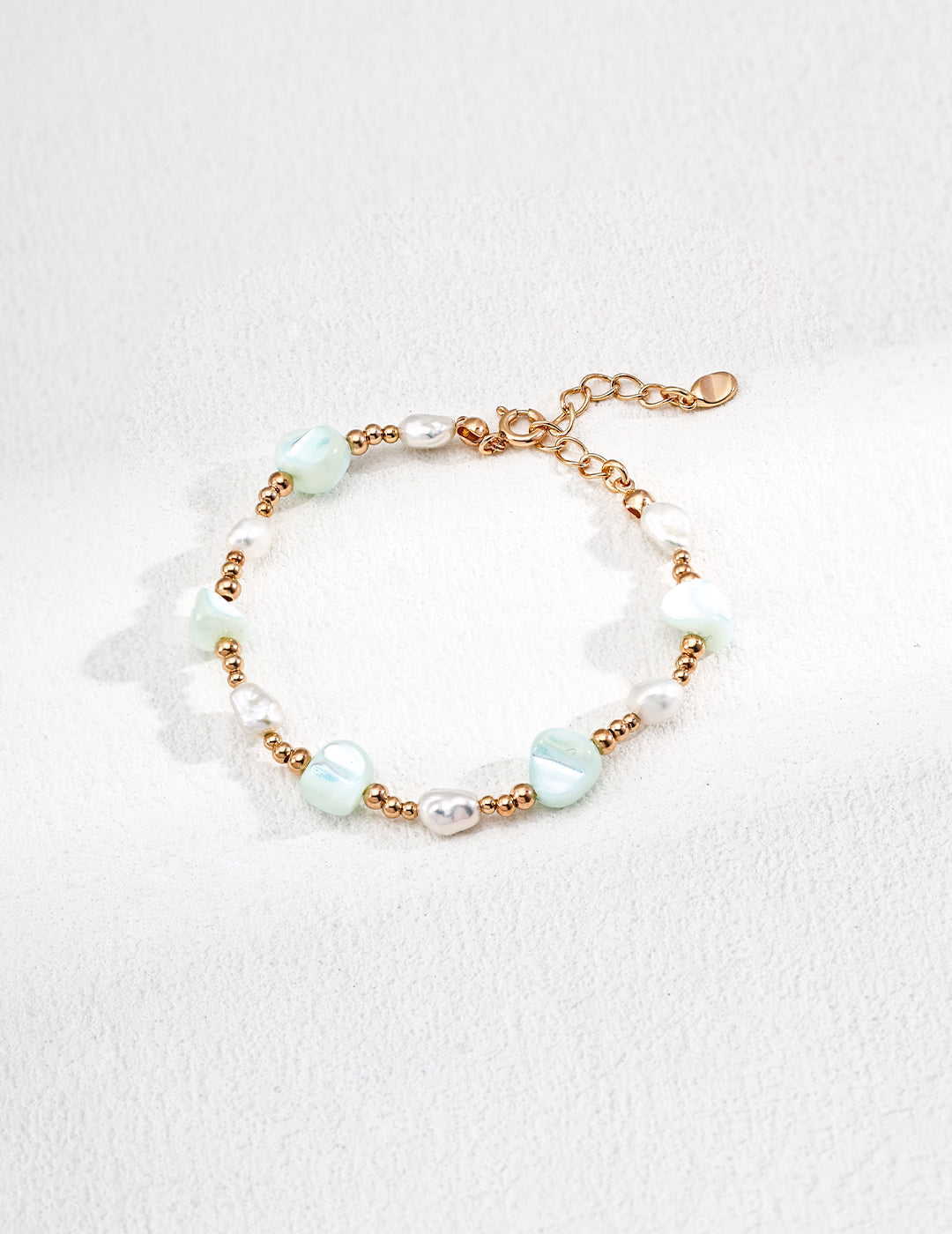 Elegant bracelet made of green and white beads, adorned with freeform shells and freshwater pearls for a stylish look.