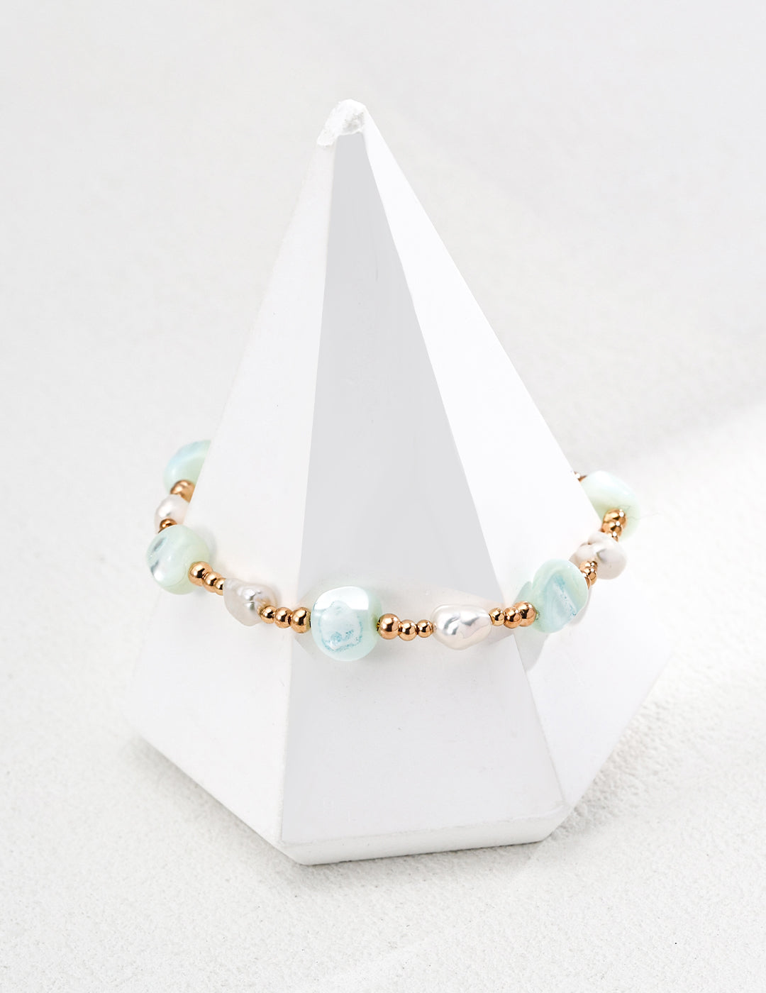 A bracelet featuring green beads, gold accents, freeform shells, and freshwater pearls.