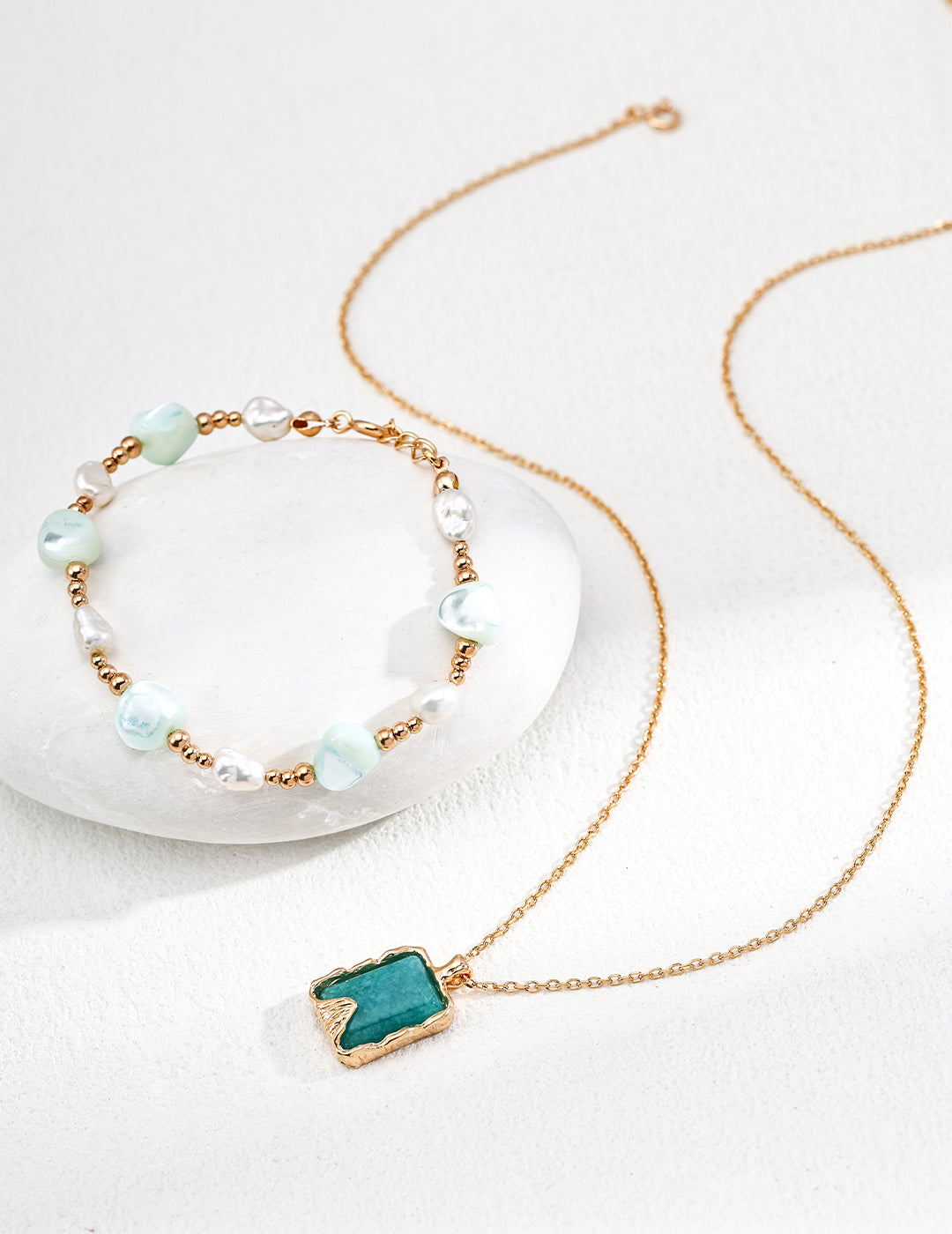 Necklace with a pendant, paired with a bracelet of freeform shells and freshwater pearls on a white surface.