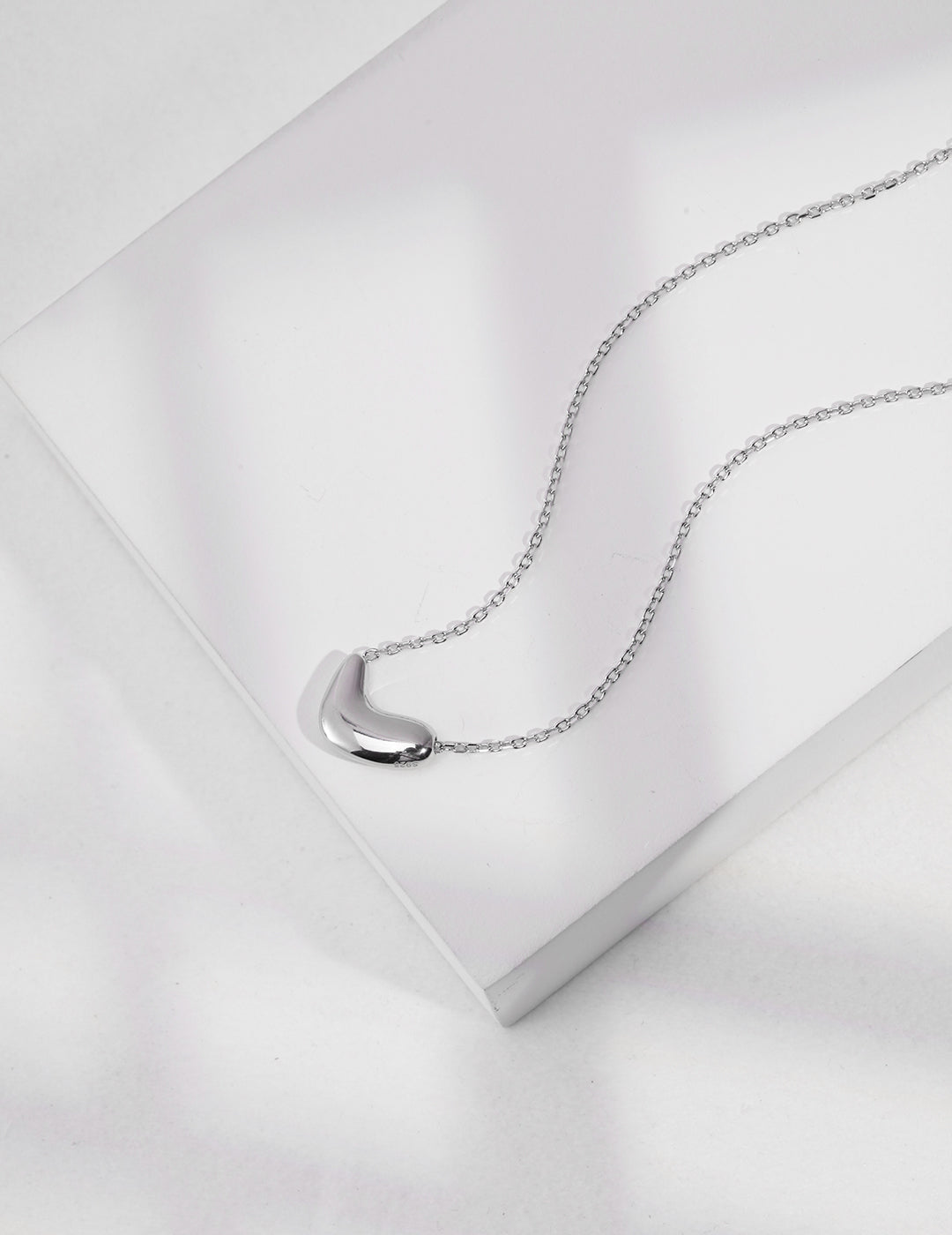 A chain necklace with a curved shape on top, featuring a silver bean pendant.