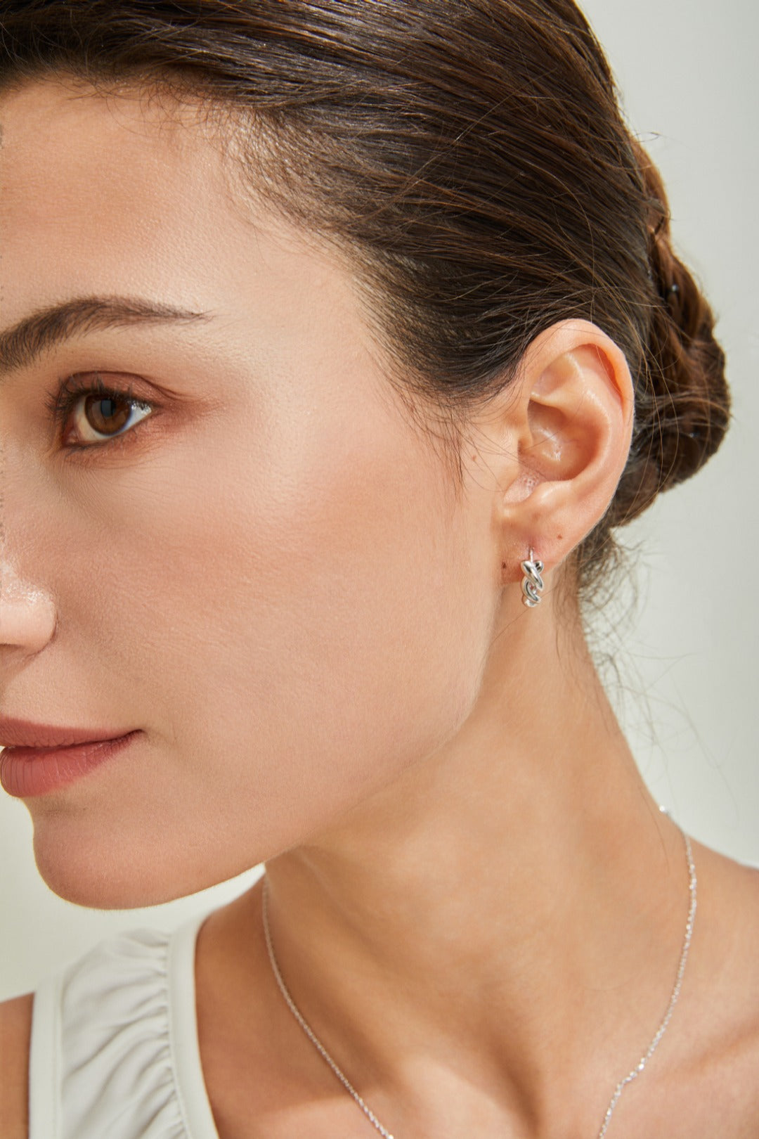 A stylish woman dons a white top and silver twisted hoop earrings, highlighting her fashionable look.