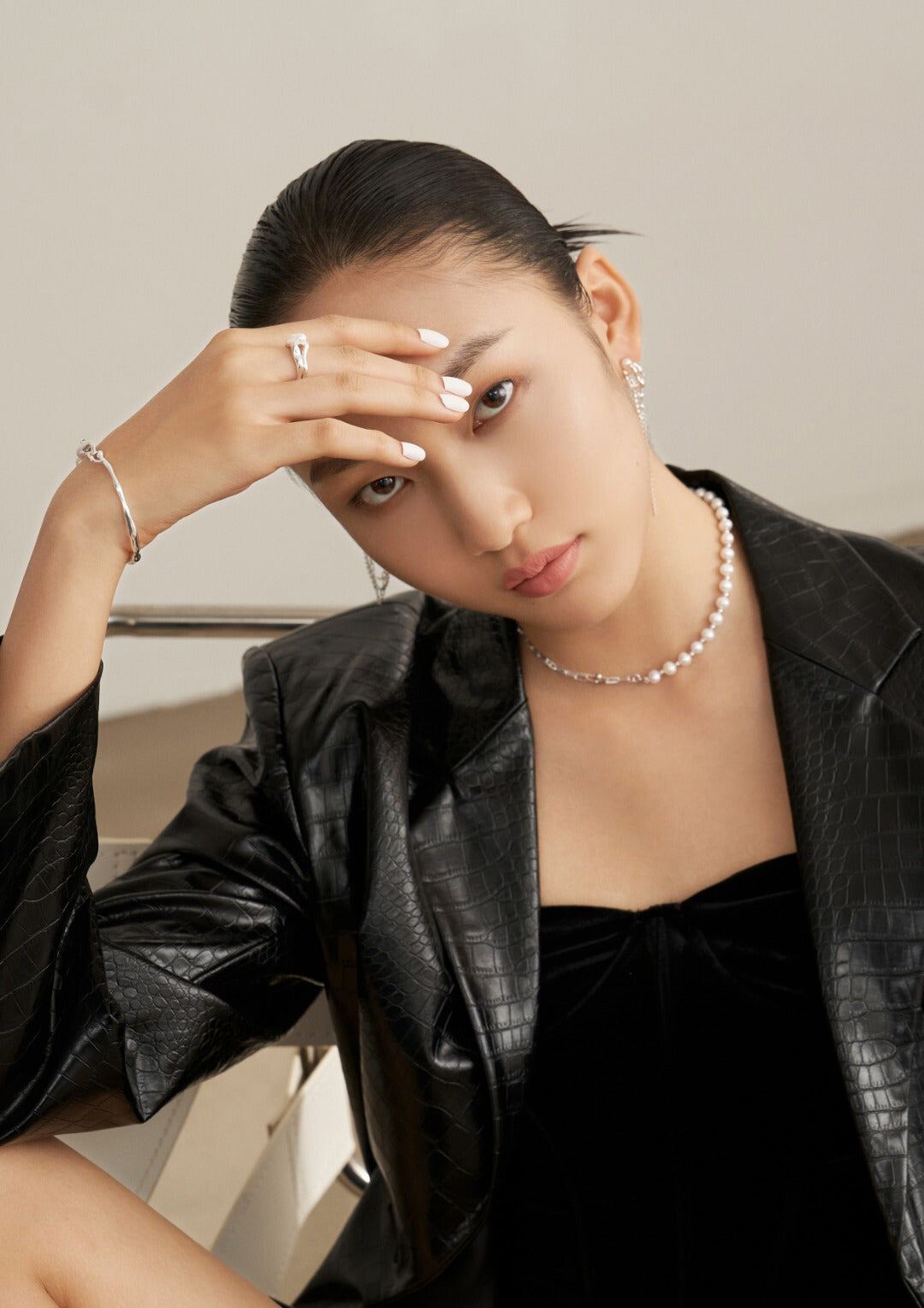 Woman in black jacket sitting on chair, wearing silver necklace with half pearls and half gold chain design.