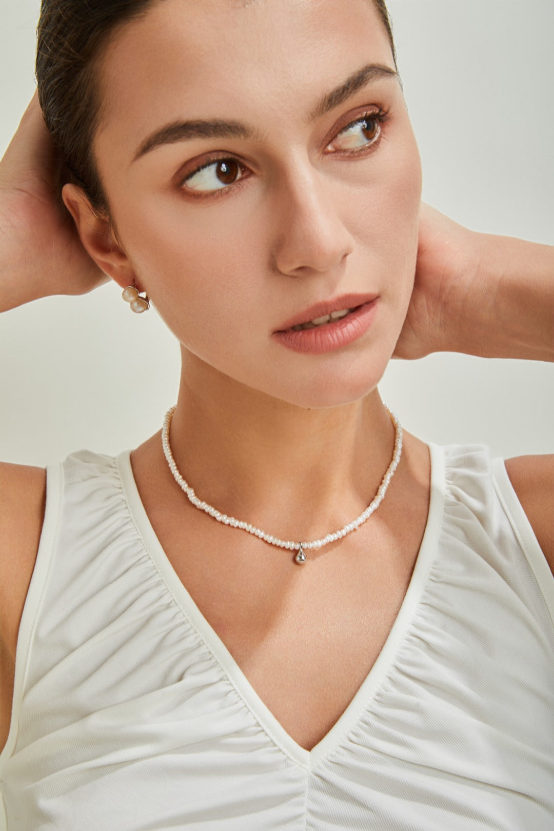 A woman wearing a white top and a necklace, radiating sophistication and grace in her appearance.