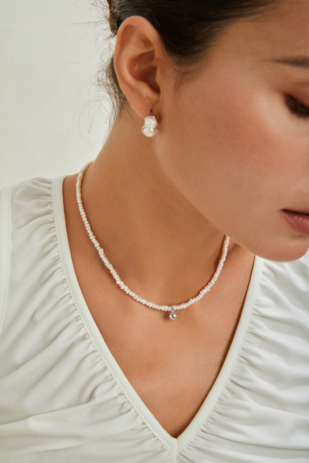 A woman in a white shirt and pearl necklace, exuding elegance and sophistication.