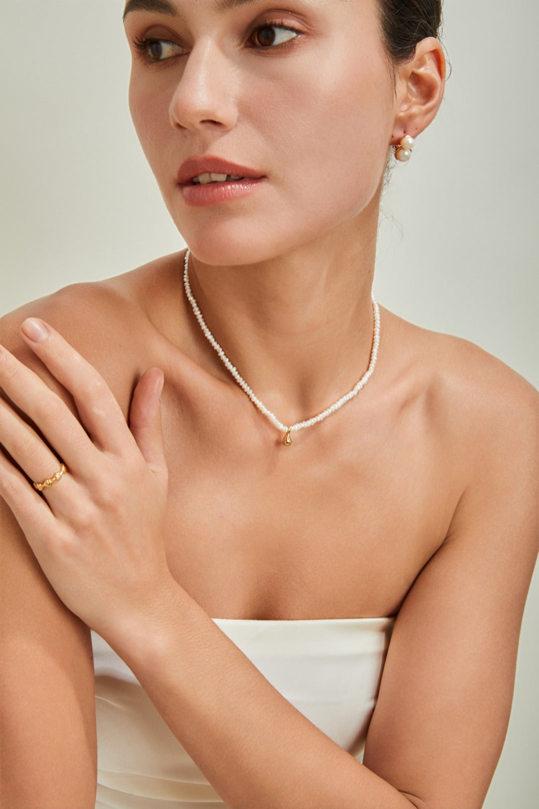 A stylish woman wearing a white dress and a necklace, radiating sophistication and charm.