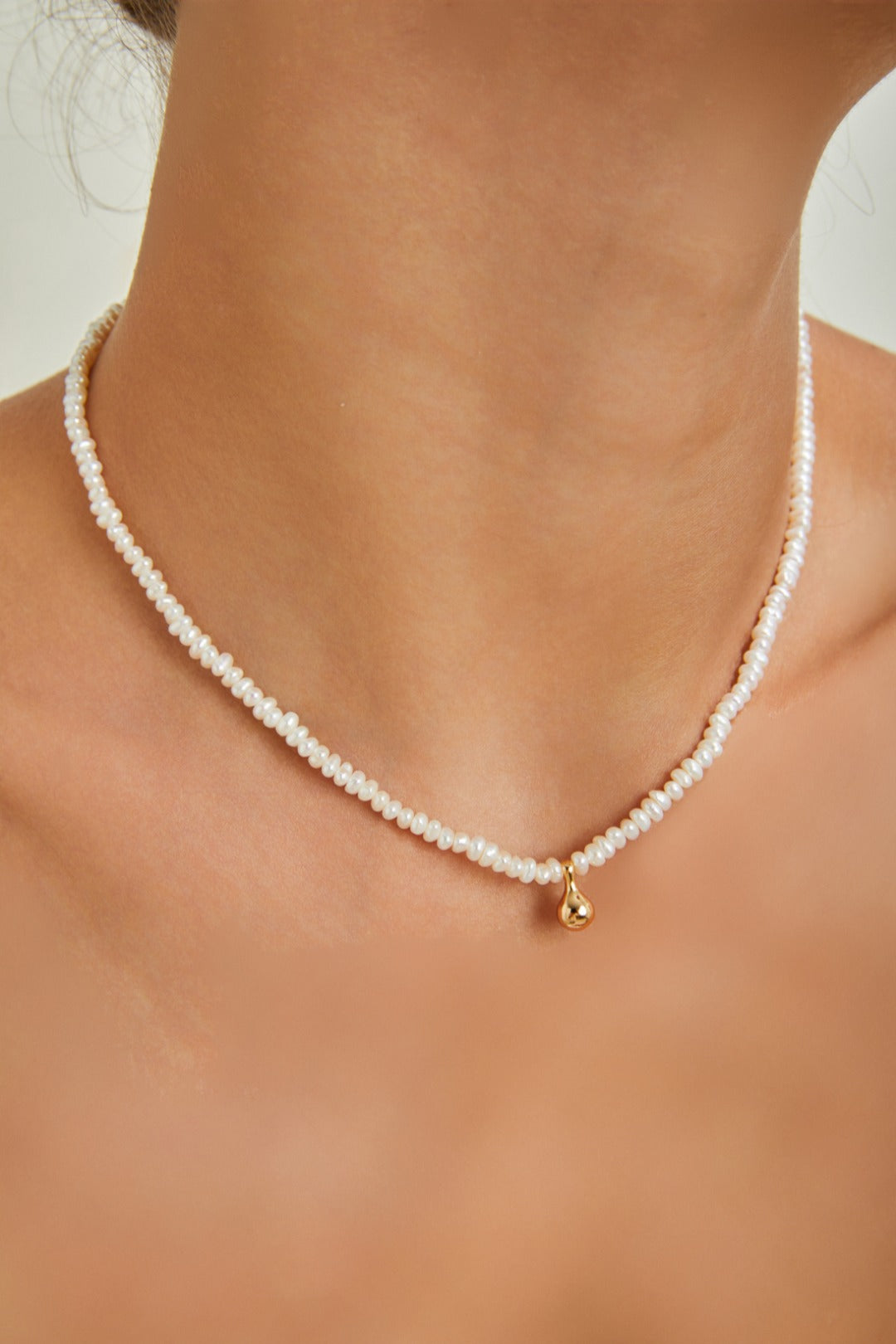 A woman showcasing a beautiful white pearl necklace paired with a chic gold charm, radiating elegance and style.