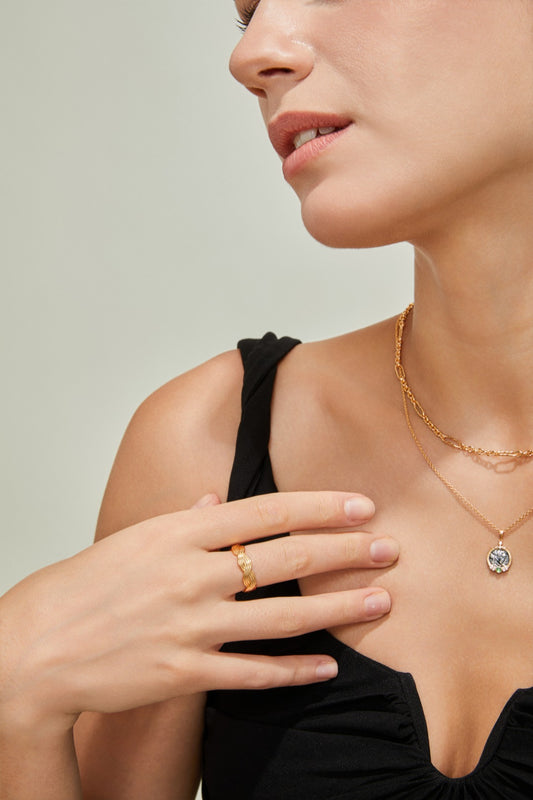 A woman elegantly wears a necklace and a braided gold ring, emphasizing her fashionable accessories and personal style.