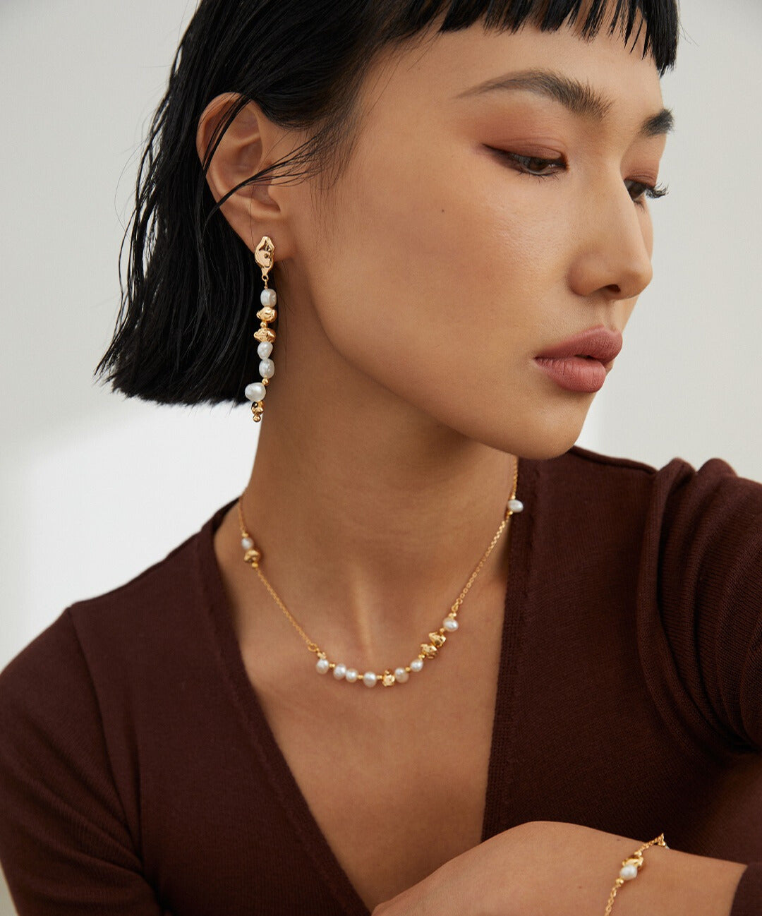Woman wearing baroque pearl dangles from Mezuille, layered with necklace and bracelet.