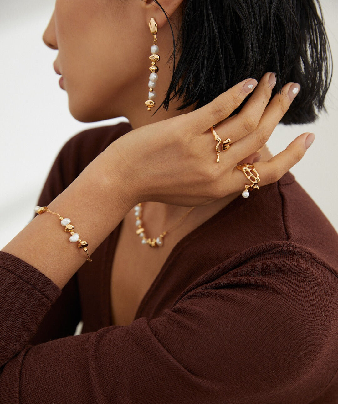 A woman showcasing her elegance with a gold bracelet and earrings, including gold plated baroque pearl beads and assorted jewelry.