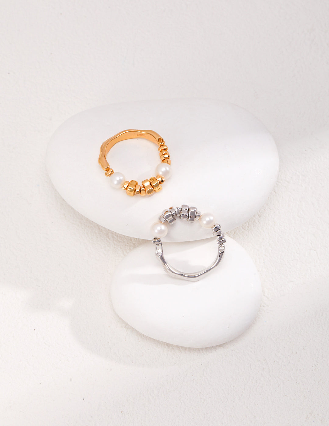 Two silver and gold pearl rings placed on top of white stones.
