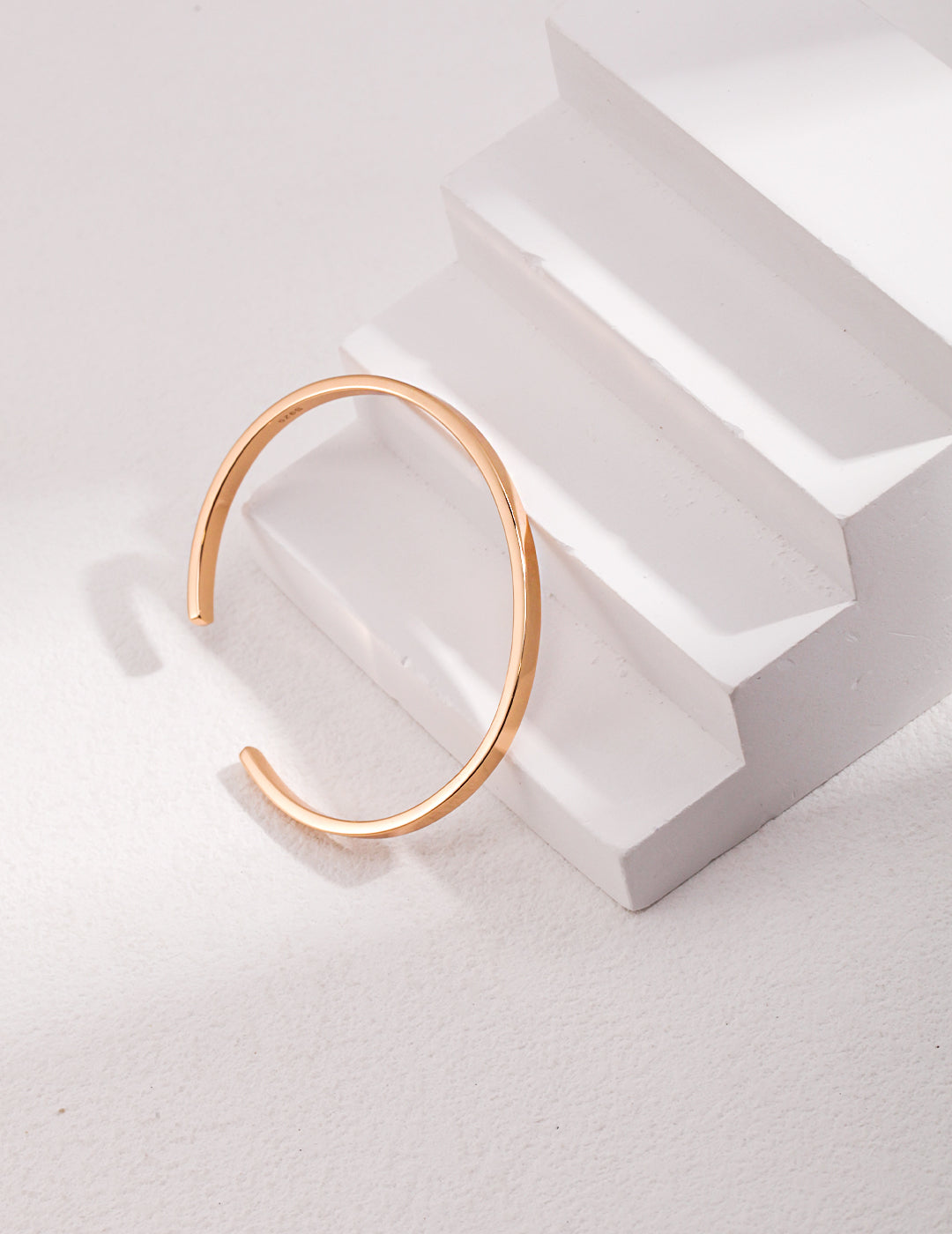 A gold bangle bracelet resting on a white surface, radiating elegance and sophistication.
