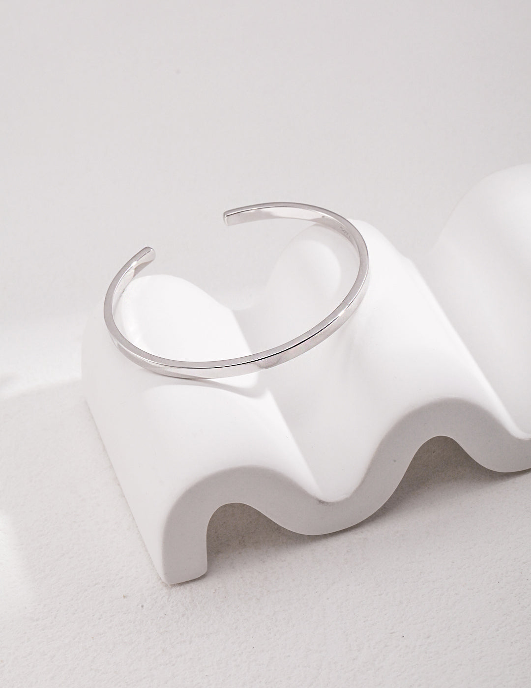 A silver bangle bracelet resting on a white surface, adding elegance and style to any outfit.