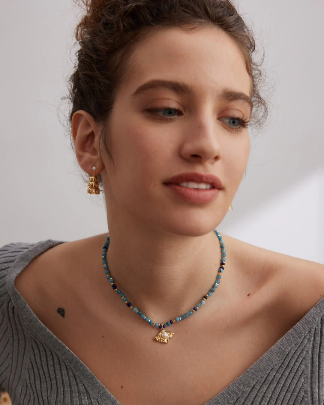 A woman showcases an aquamarine necklace adorned with a striking blue stone.