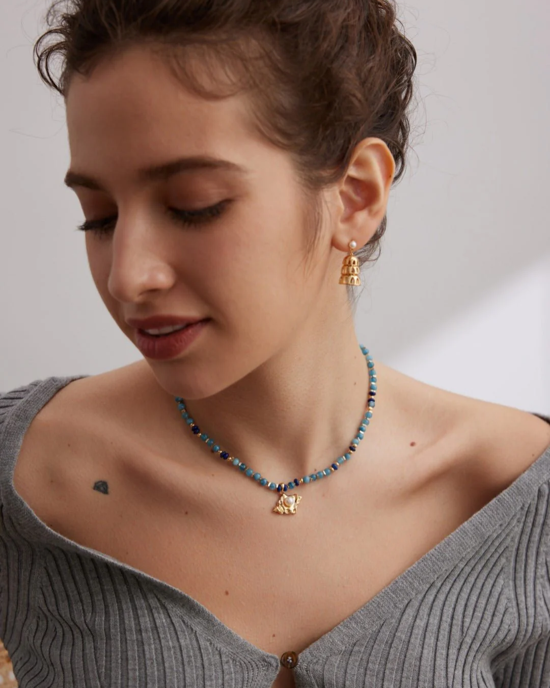 A woman displays an aquamarine necklace with a gold and blue stone, adding a touch of sophistication to her look.