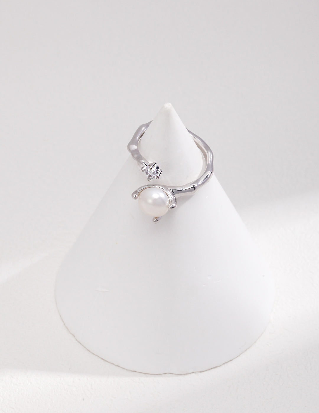 Elegant silver wrap ring with a white pearl and cubic zirconia, resting on a white cone.
