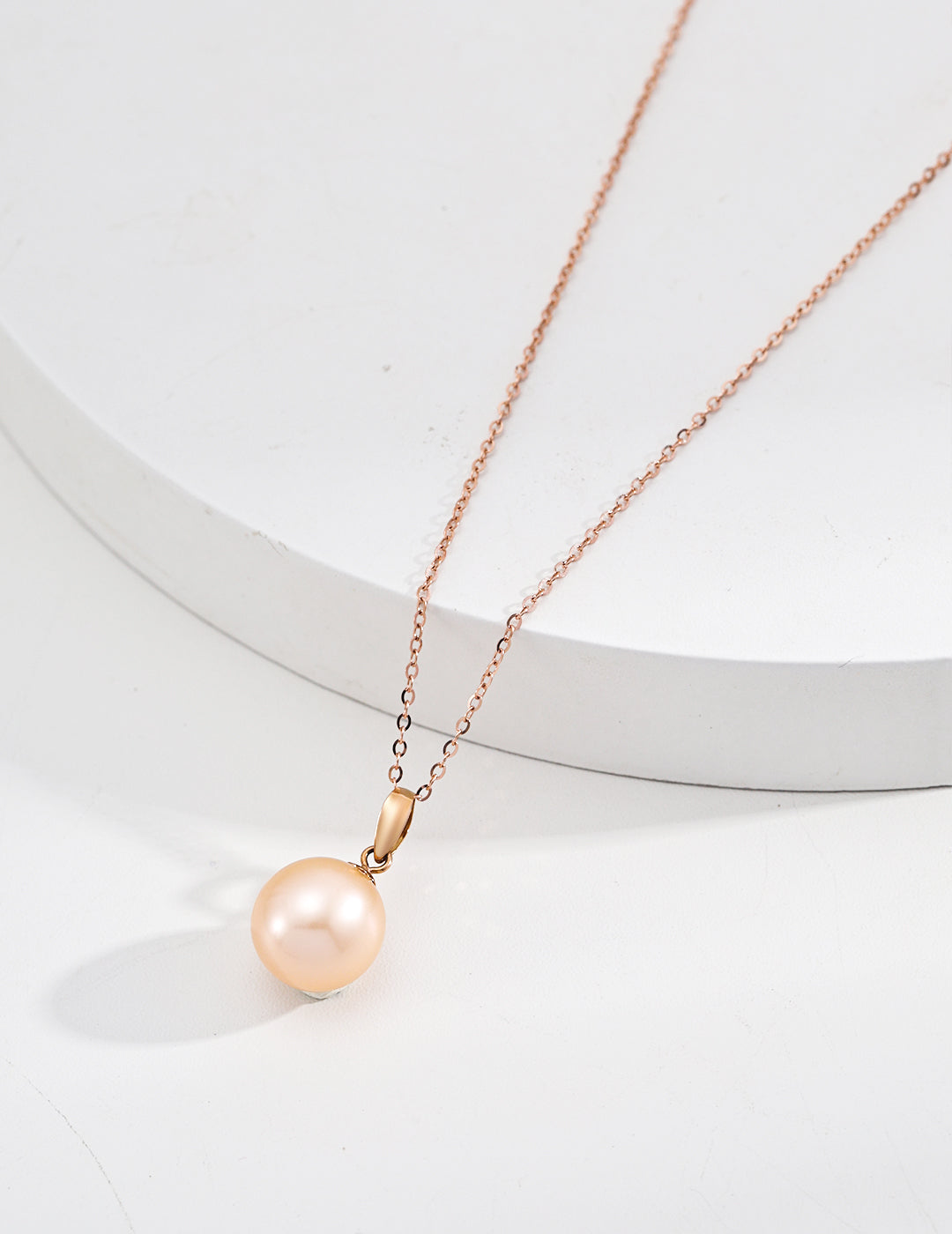 A rose gold freshwater pearl pendant elegantly hangs from a delicate karat gold chain.