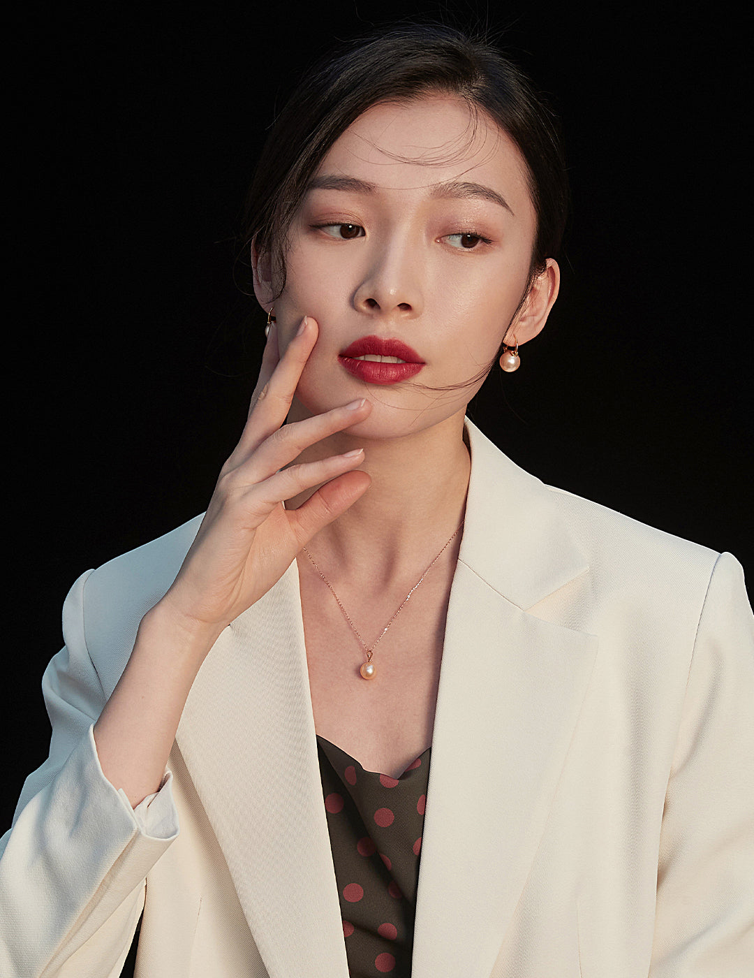 A fashionable woman dons a white blazer and polka dot dress, complemented by a stunning rose gold freshwater pearl necklace.