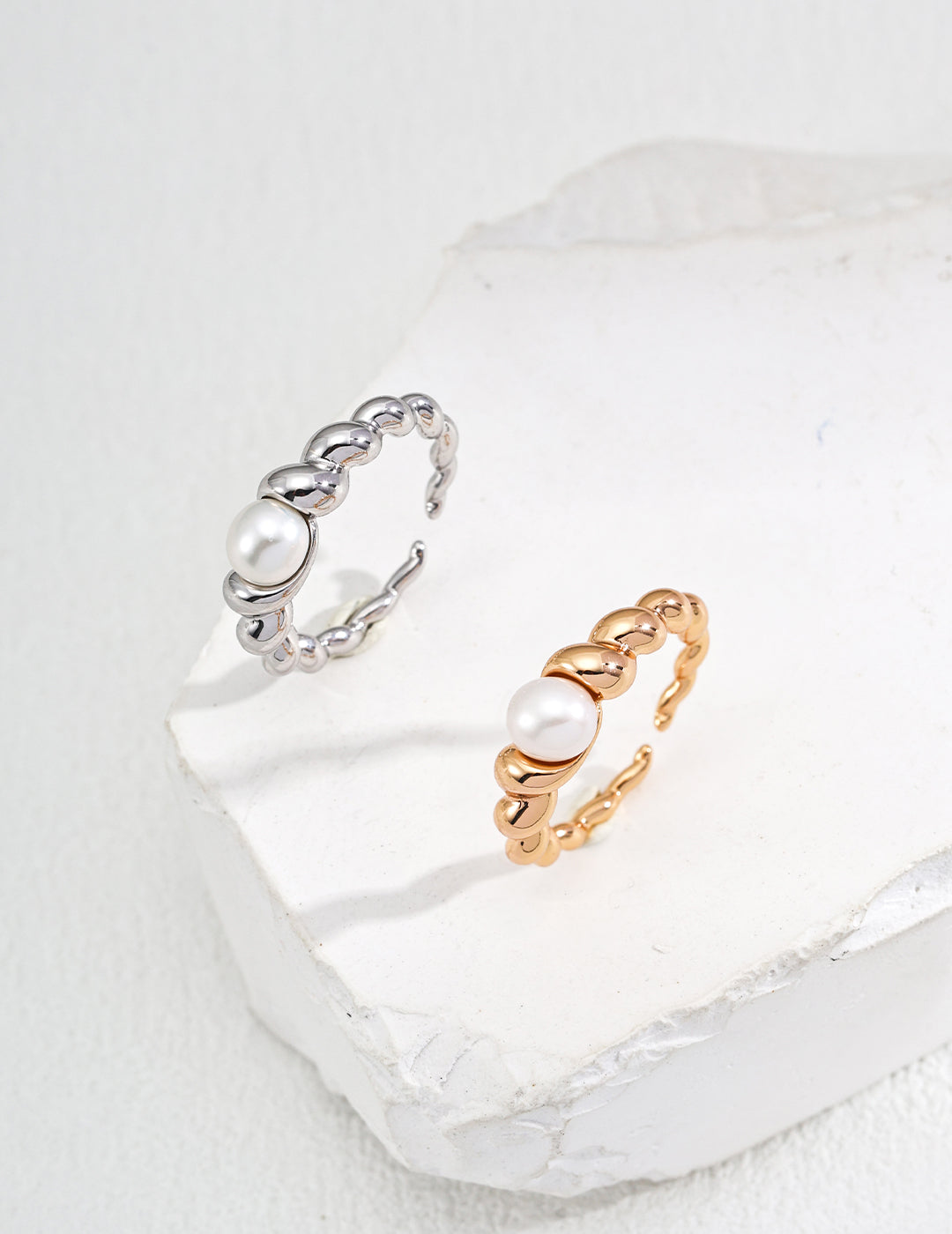 A pair of stylish rings with gold and silver stones resting on a white surface, offered in silver or gold finishes.