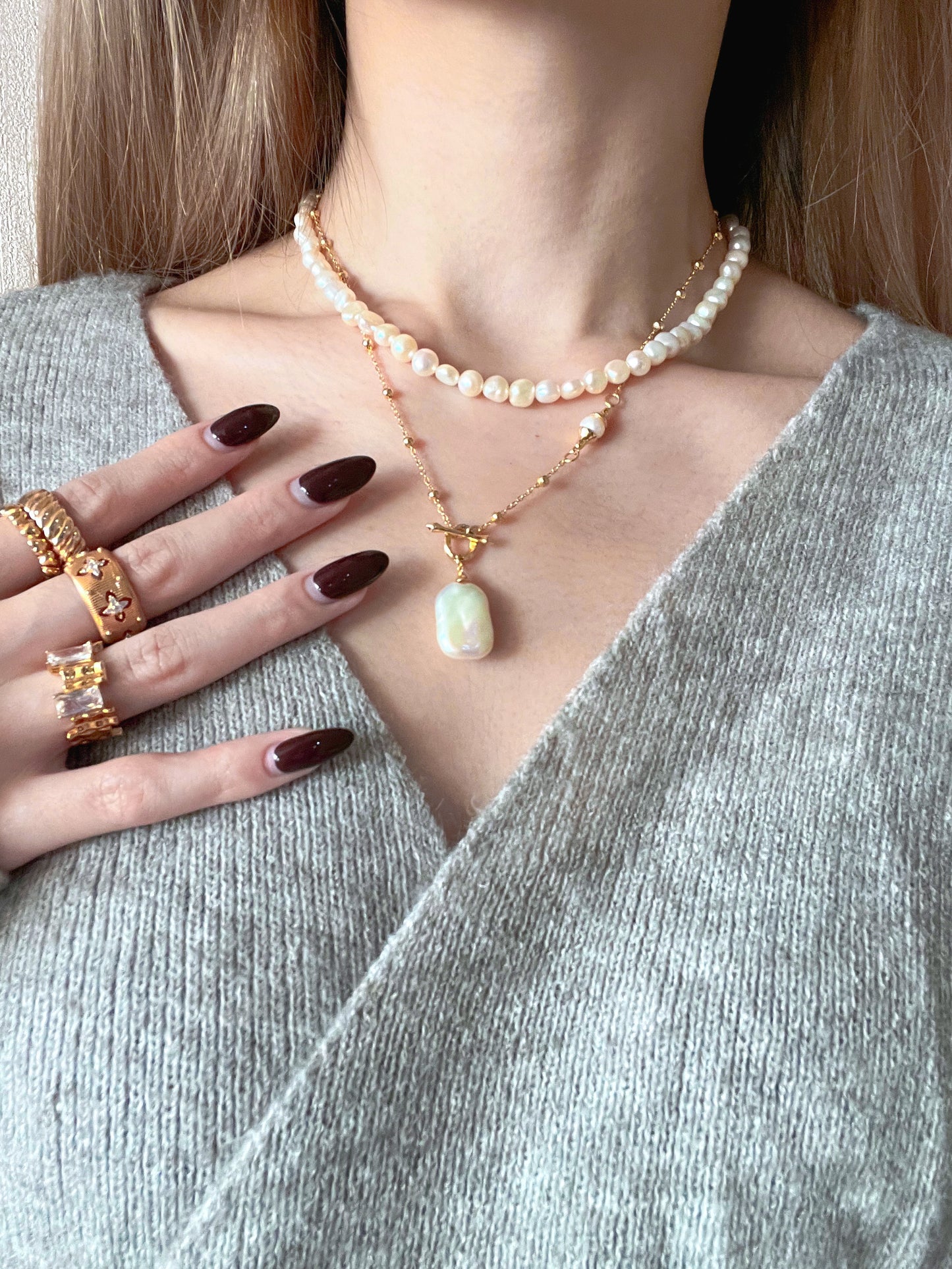 A woman adorned with a pearl necklace and several rings, exuding sophistication and charm.