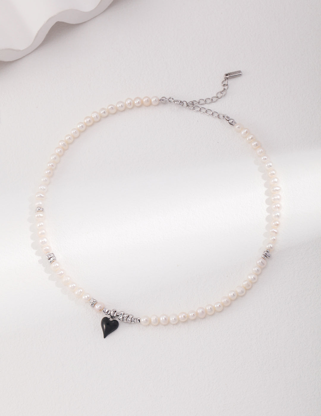 Elevate your look with a silver necklace showcasing freshwater pearls and a black heart pendant, a stunning combination of elegance and edginess.