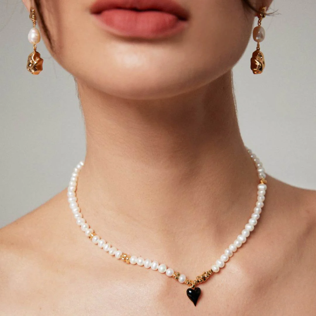 A woman wearing a heart-shaped necklace adorned with pearls and gold.