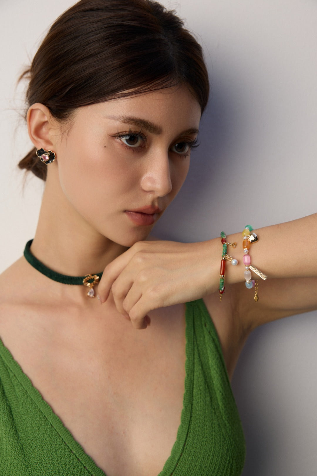 A woman in a green dress shows off a colorful rainbow cat's eye bracelet, smiling as she poses for the photo.