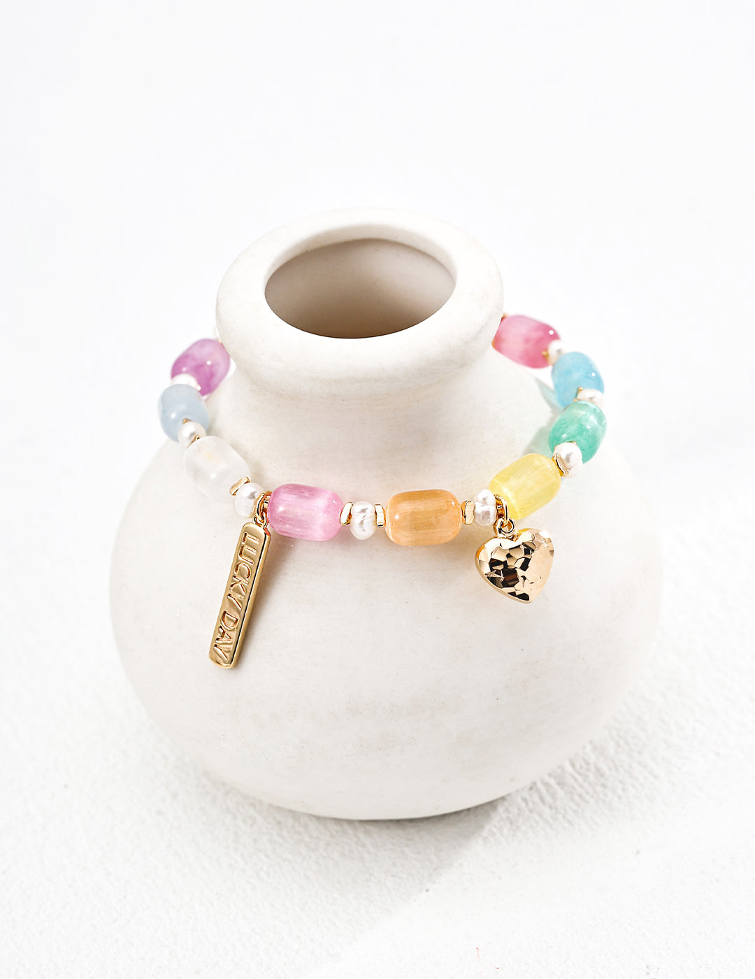 A white vase adorned with a multicolored cat's eye bracelet in bright rainbow hues.