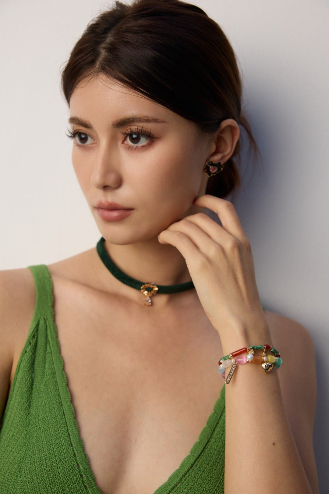 A woman in a vibrant green dress, showcasing a rainbow-hued cat's eye bracelet on her wrist.