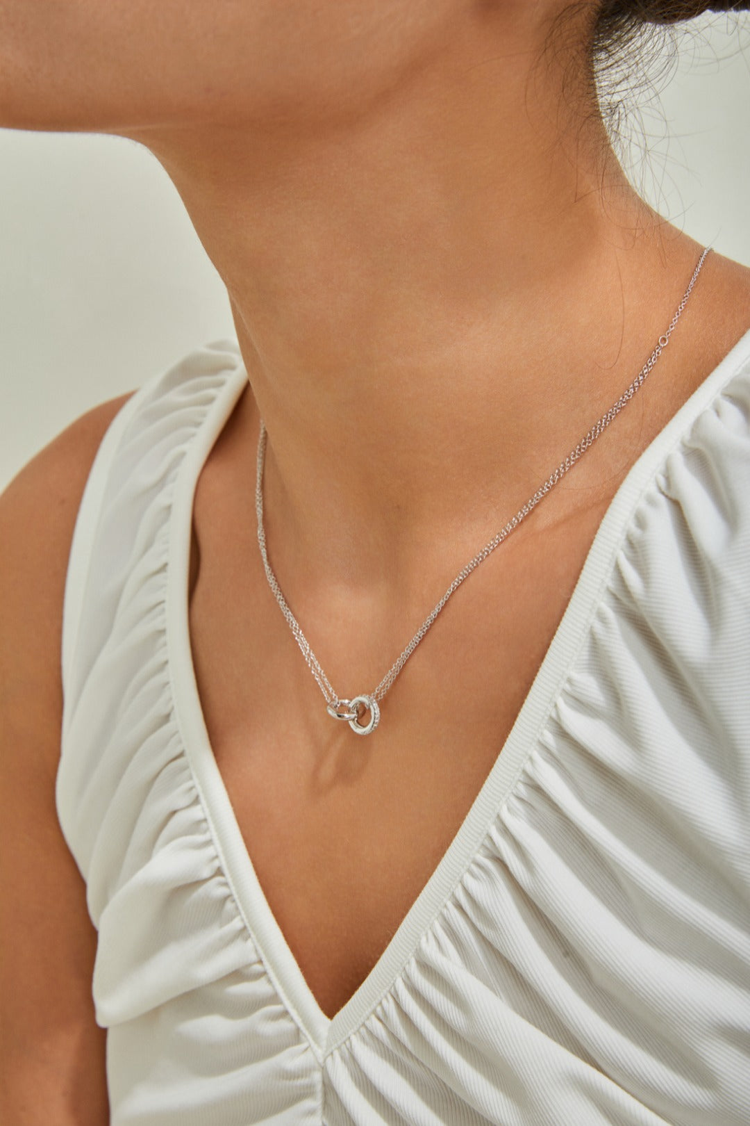 A woman elegantly dressed in a white top, adorned with a diamond heart necklace, embodies beauty and charm.